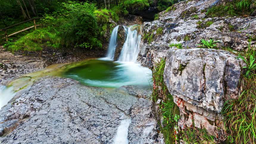Waterfall falls between rocks forming a green water pool