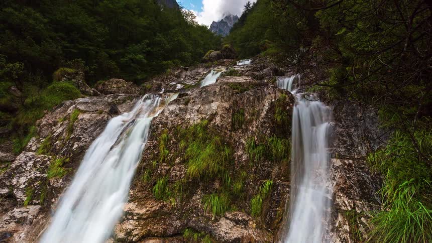 Waterfall flows down rocks among trees in a mountain valley