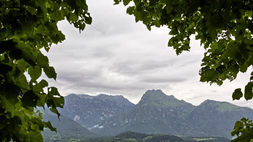 View of mountains through the trees as clouds move across the sky