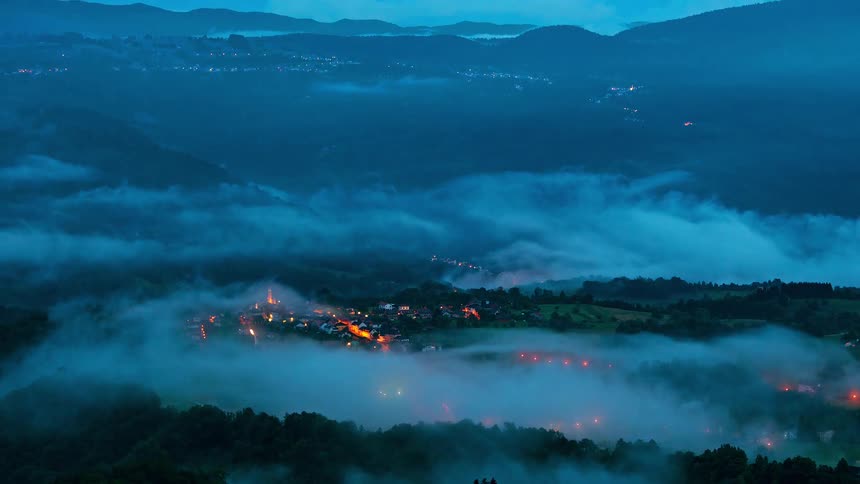 Village illuminated at night surrounded by fog among hills