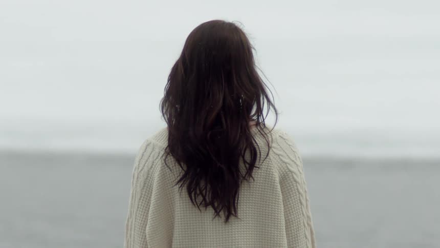A woman in a white sweater is walking on the beach