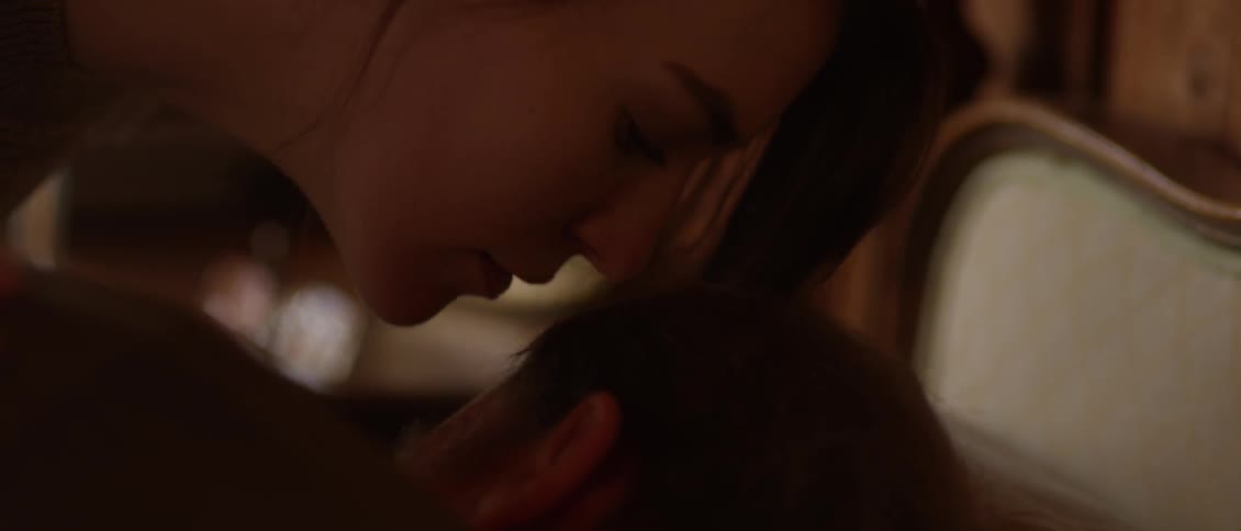 A woman leans over a person sleeping and kisses them