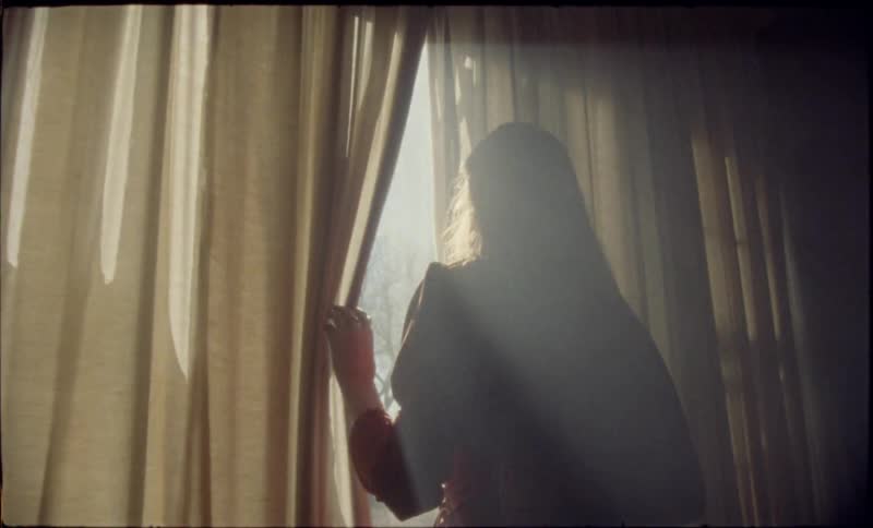 Woman opens a curtain and looks through a sunlit window