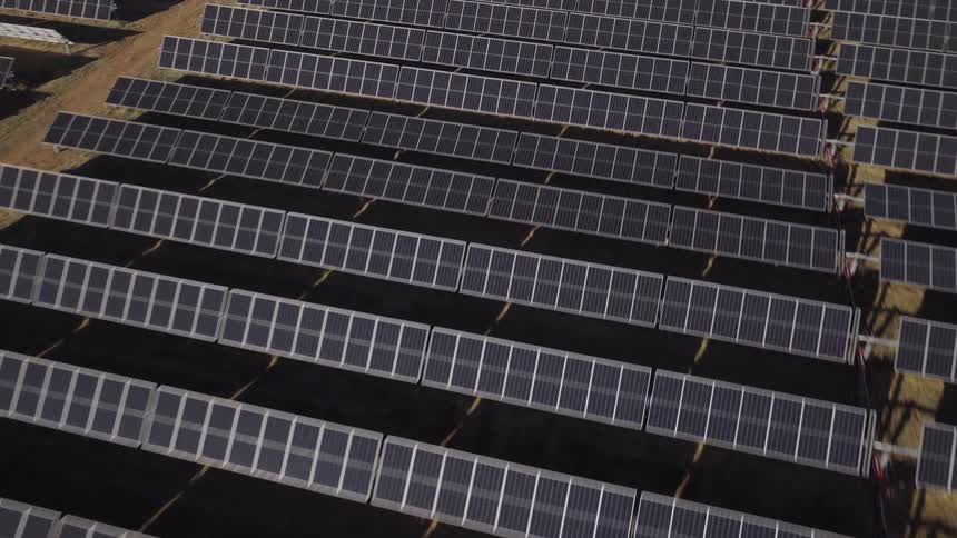 Rows of solar panels stand on dark ground at a solar farm during the daytime