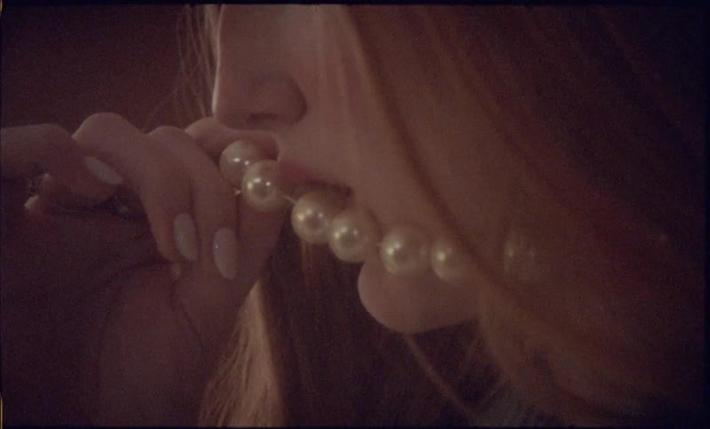 Closeup of a woman biting a pearl necklace near her lips in warm soft indoor lighting