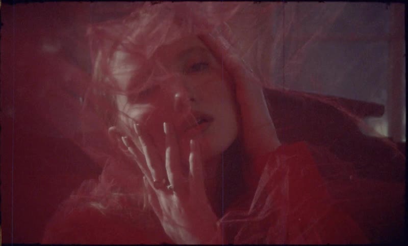 A young woman gazes forward while covered in a translucent red fabric