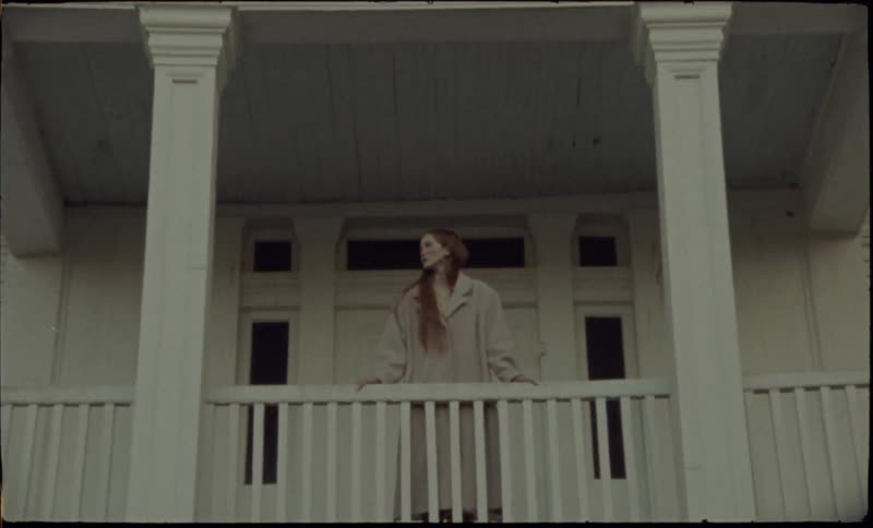 Woman stands on the balcony of a house with white columns