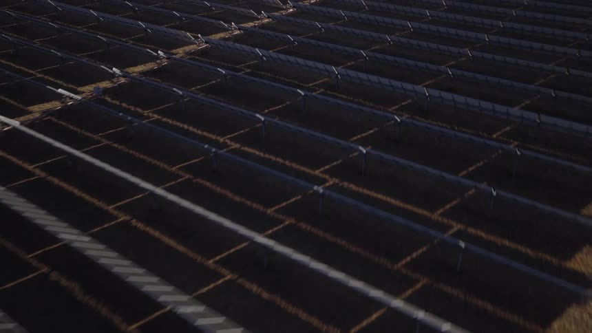 Aerial view of rows of solar panels across a desert farm with the surrounding desert fading into the background