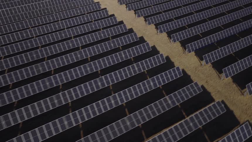 An aerial view shows a large field filled with long rows of solar panels