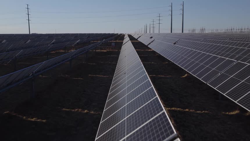 An aerial view shows a large field filled with long rows of solar panels