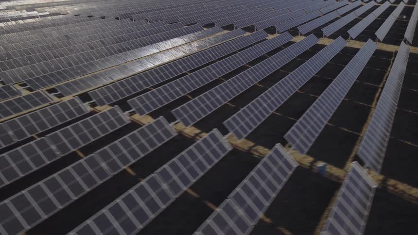 An aerial view shows a large field filled with long rows of solar panels