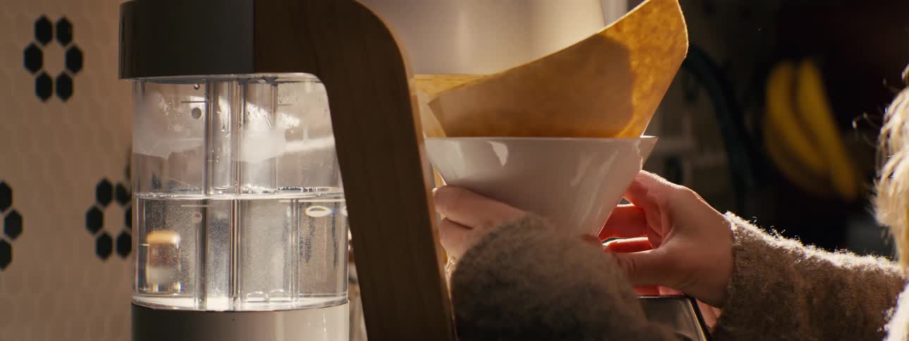 Person holds a coffee filter over a container beside a coffee maker