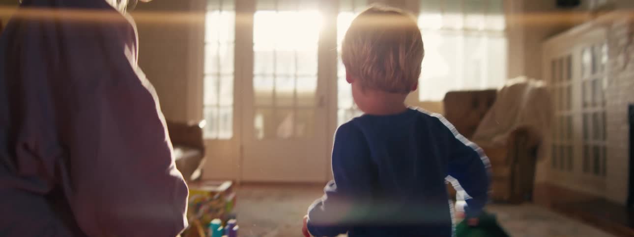 A young child picks up a bag of coffee from the floor and runs through a home with an adult