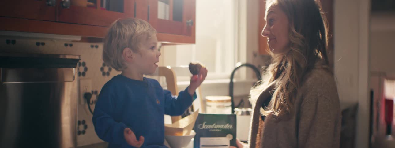 Child eats cake while woman watches in the kitchen
