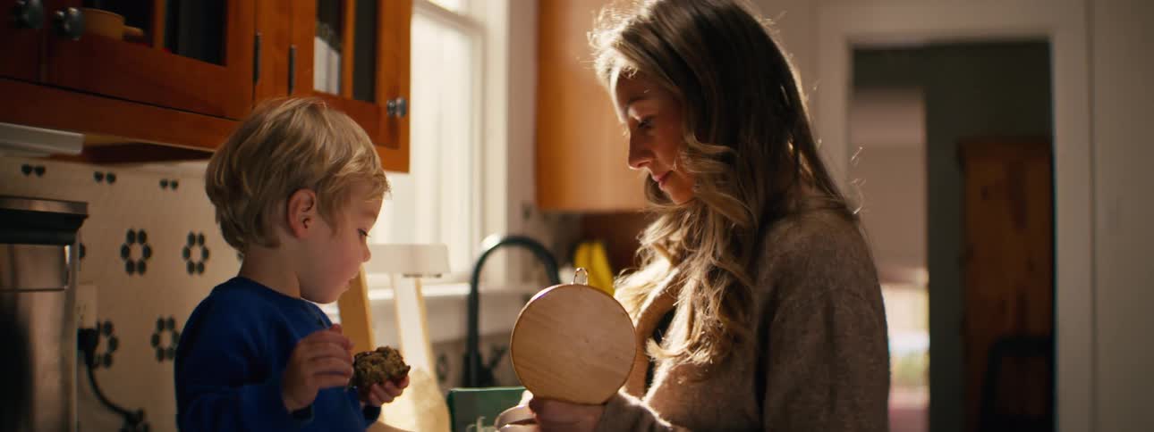 Mother and son stand together in the kitchen while the child holds cake