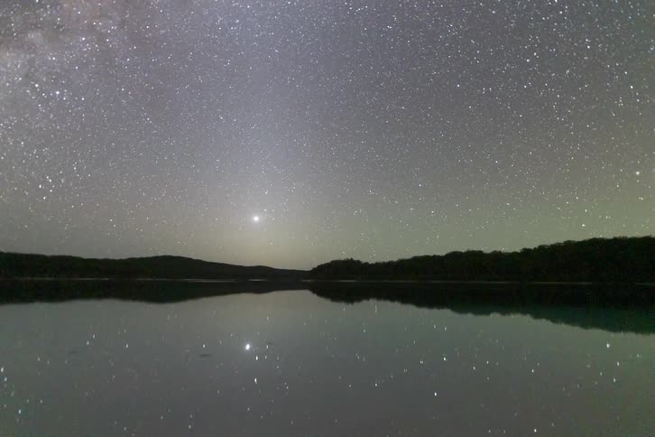 This timelapse video shows the milky way and a vast field of stars rotating across a dark night sky the celestial display is mirrored perfectly in the calm still waters of a lake as the first light of dawn begins to appear on the horizon