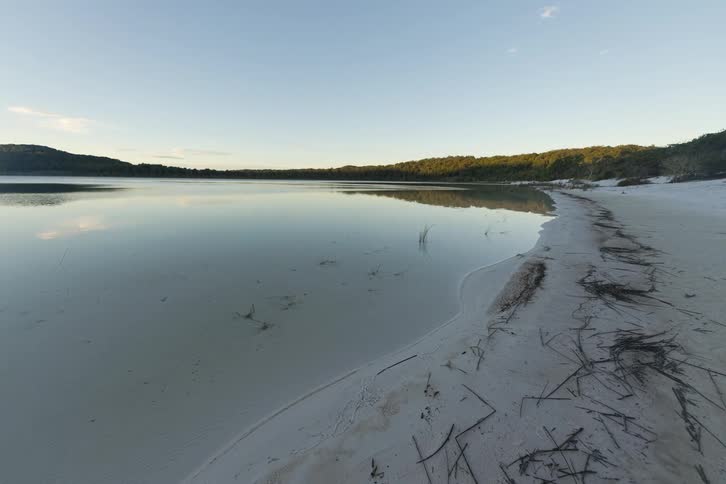Forested mountains and a beach along the coast as clouds move across the sky and reflect on the water