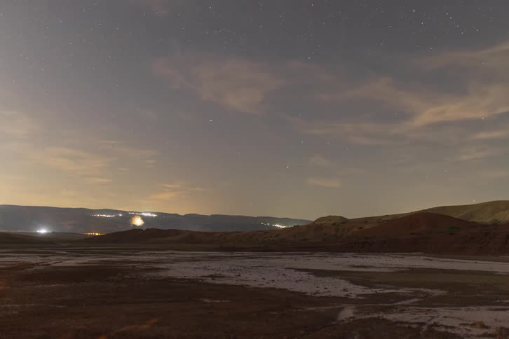 A time lapse captures stars moving across the night sky above a desert landscape with distant city lights