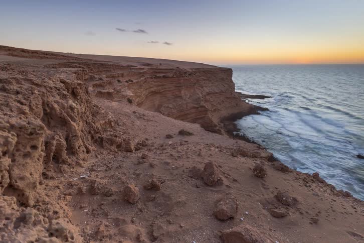 Aerial view of a rugged sandy cliff overlooking a calm ocean during golden hour sunset