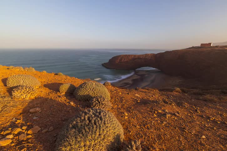 A wide angle view captures the legzira beach stone arch at sunset from a rocky cliffside perspective