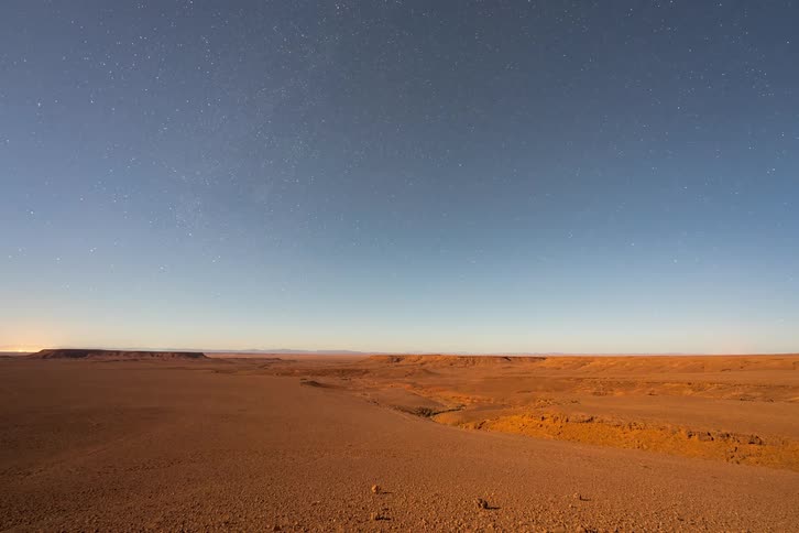 A time lapse captures the transition from twilight to night showcasing the milky way above a desert landscape followed by a sunrise