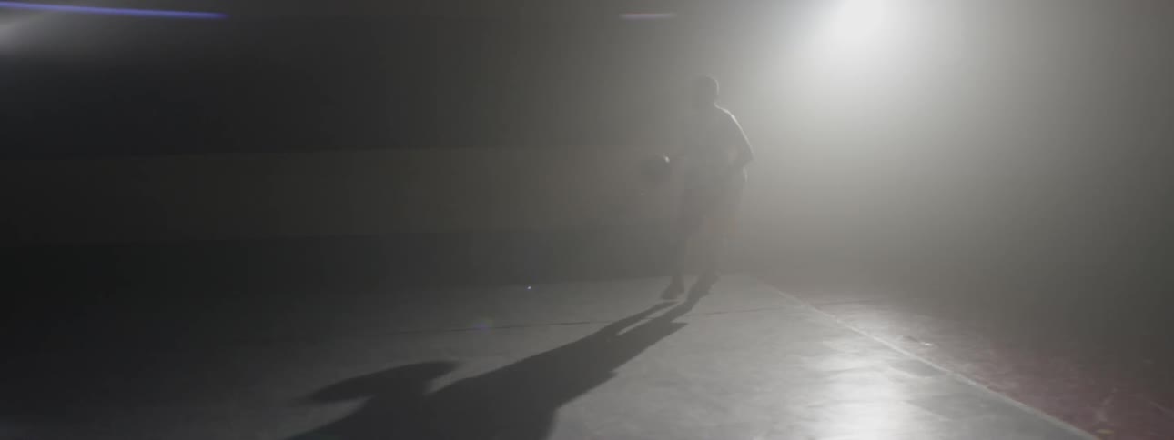 Young man shooting a basketball around on a dark indoor court
