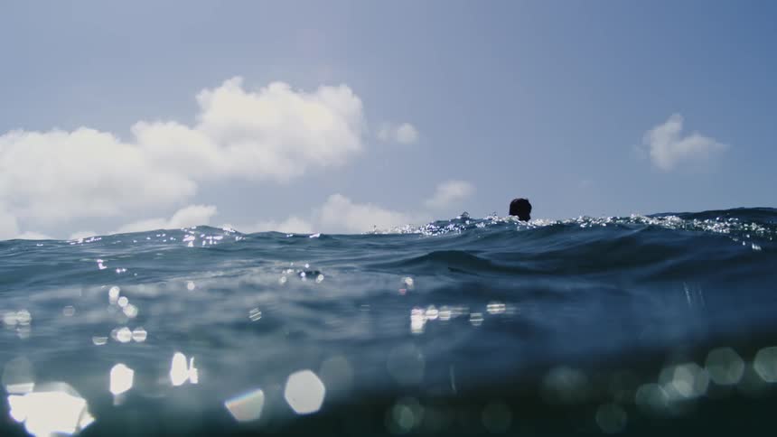 Sunlight shines on the water as a man swims and the view moves underwater