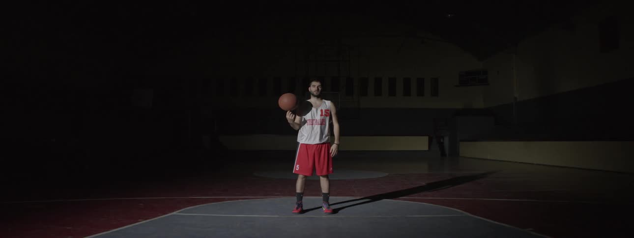 A man spinning a basketball on his finger in the middle of a court