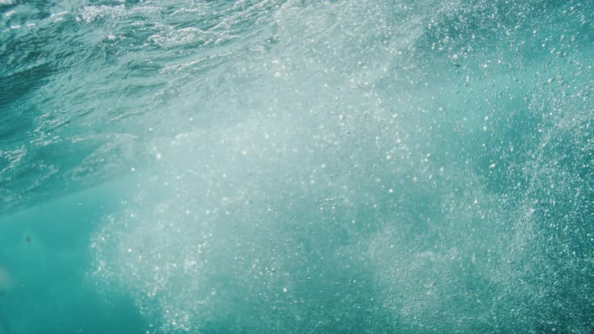 Underwater view as sunlight shines upon ripples on the water and air bubbles floating to the surface