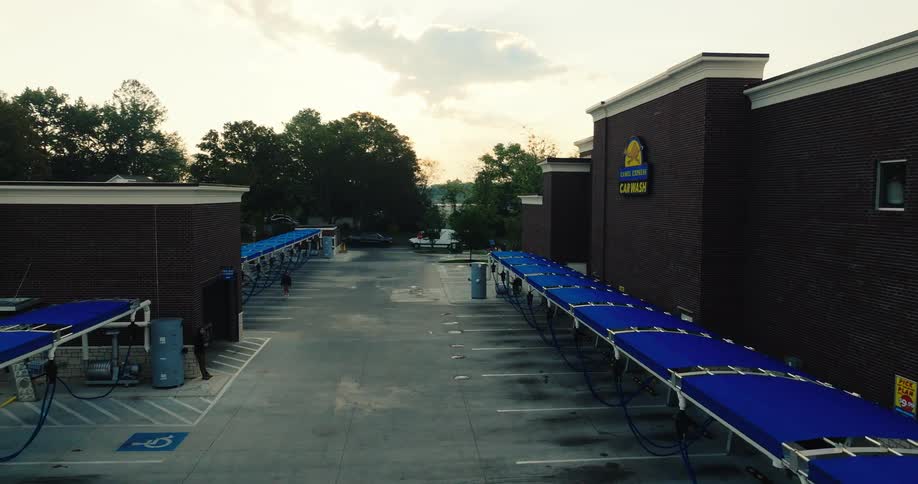 A brick car wash facility featuring long rows of blue canopies over vacuum stalls within a clean parking lot during the late afternoon