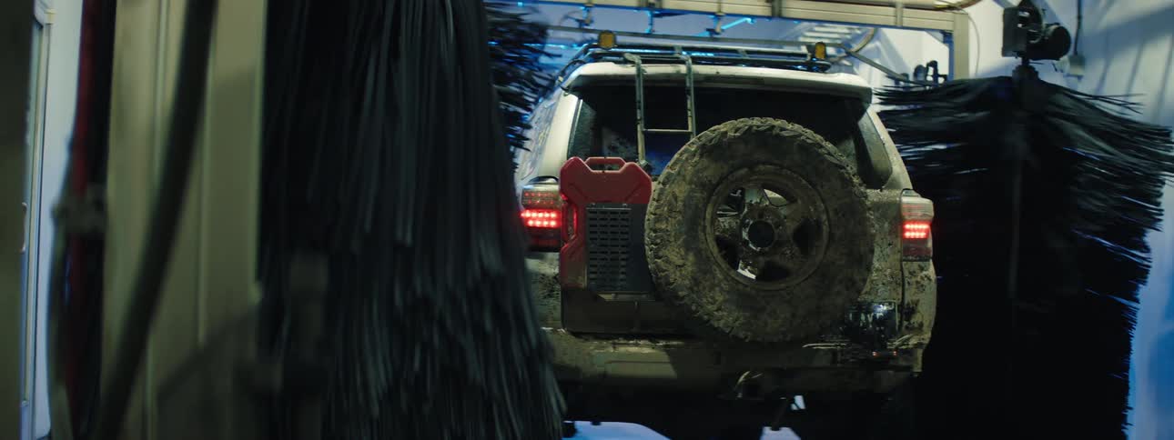 A muddy off road suv slowly moving through an automated car wash with spinning brushes cleaning the vehicle