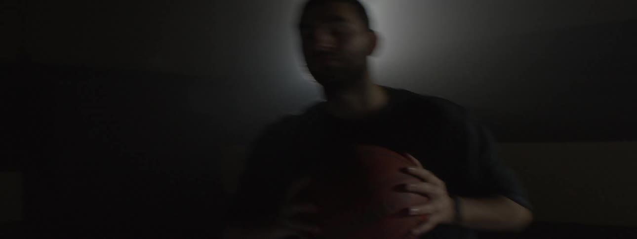 Man in a darkened room shoots a basketball and misses