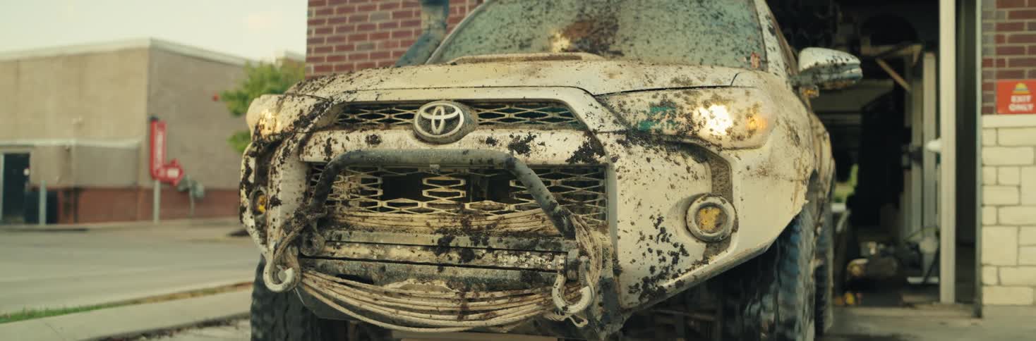 A mud covered white toyota 4runner emerges from an automatic car wash bay at a brick cleaning center