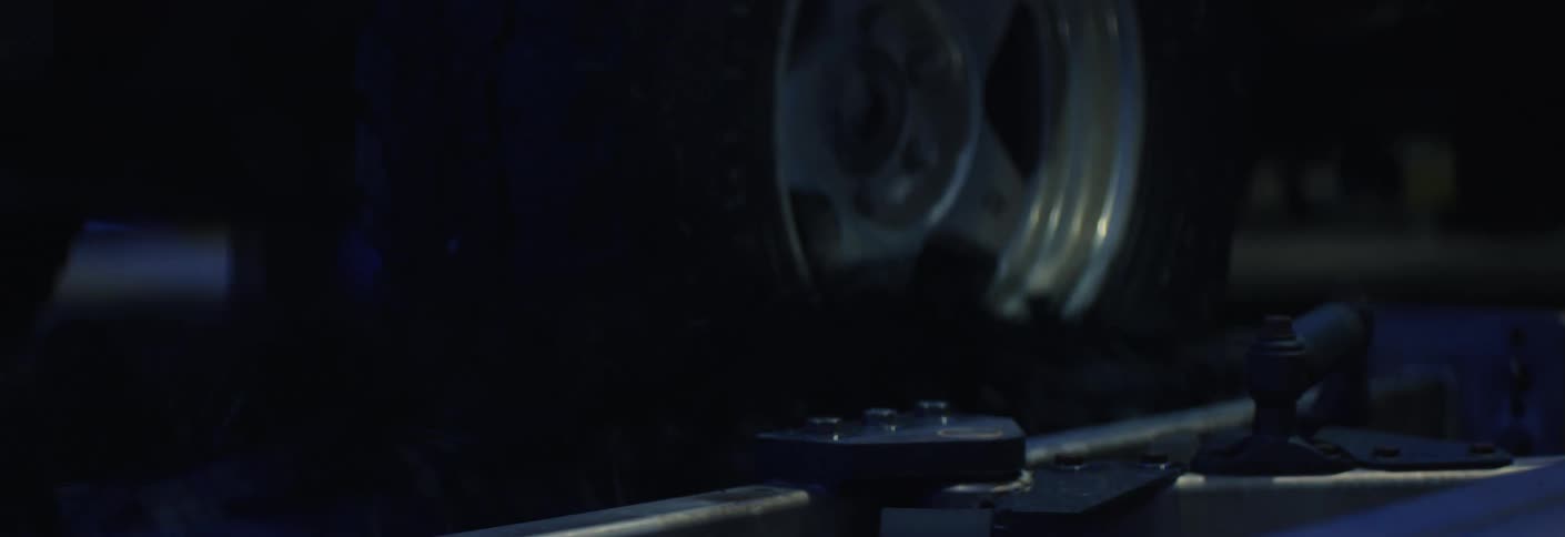 A silver wheel on a truck slowly rotates while it passes by cleaning equipment in a car wash building