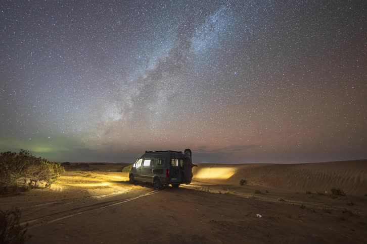 The video features a dark van parked in a vast sandy desert landscape under a transition from dusk to nightas the timelapse progresses the milky way emerges with stunning clarity rotating across the starfilled sky above the dunes