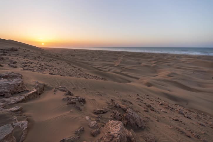 Sand covered rocks on mountains along the coast as the sun sets on the horizon