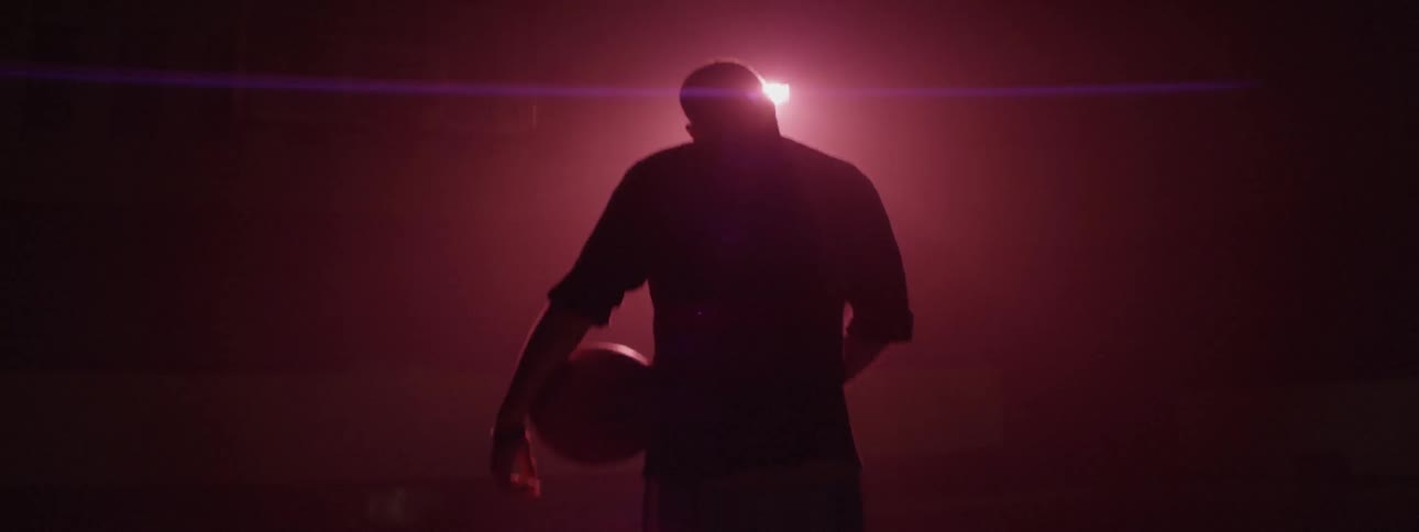 A standing man holding a basketball in red lighting