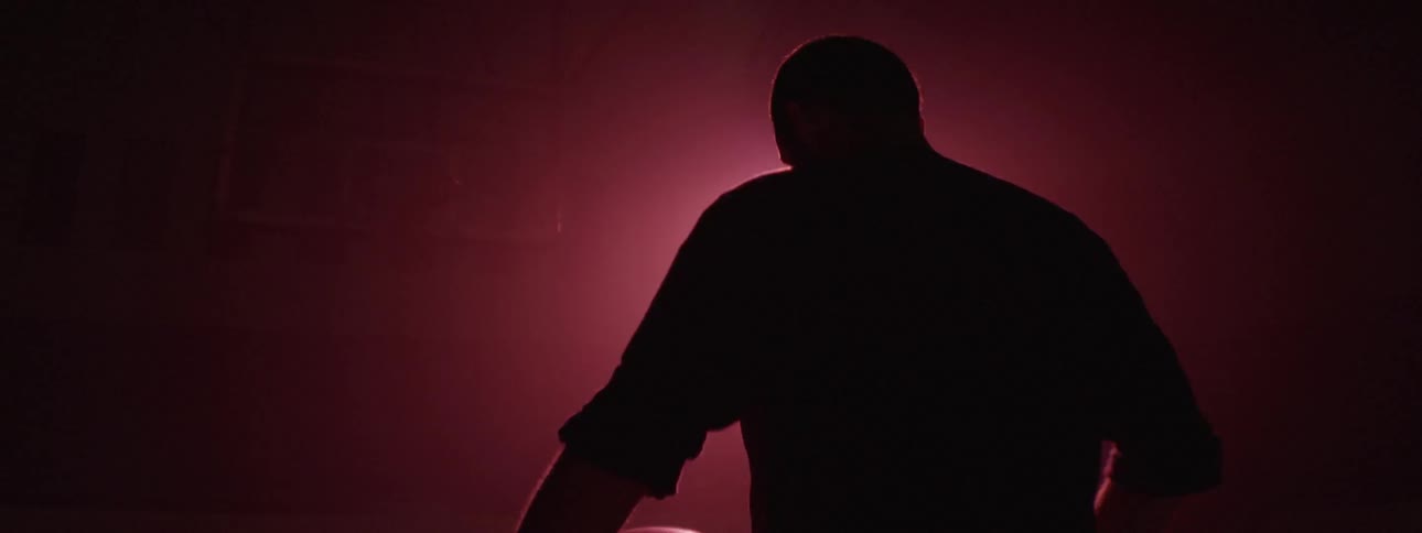 A man holding a basketball under his arm and standing on the court with a light in the background