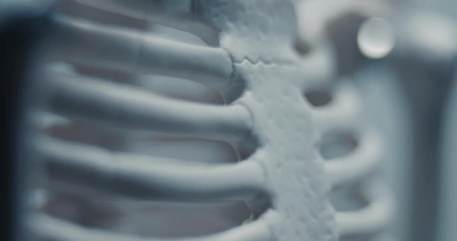 A close up shot focuses on the white rib cage and sternum of a human skeleton model under dim blue light