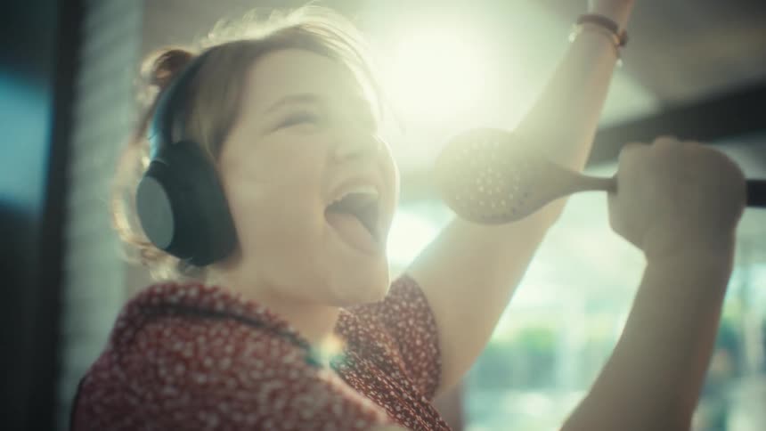 Woman wearing headphones sings using a hairbrush as a microphone while raising her arm