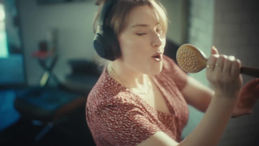 Woman singing with headphones and kitchen spoon