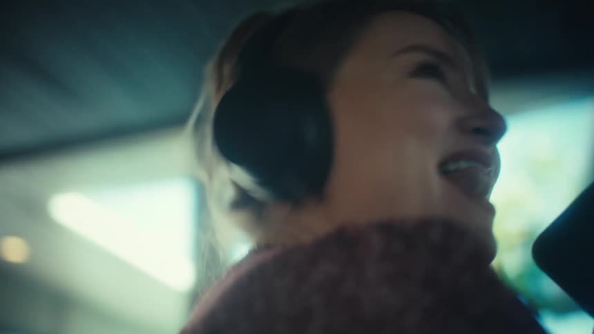 Woman wearing headphones sings into her smartphone at home during the daytime