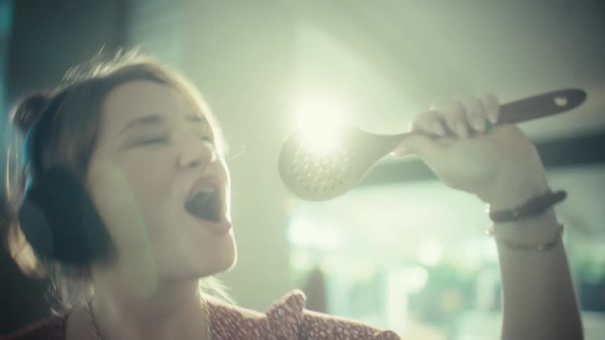 Woman singing with headphones and kitchen utensil