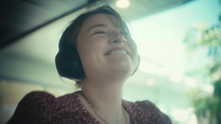 A joyful woman wearing headphones sings and dances while walking through a modern home