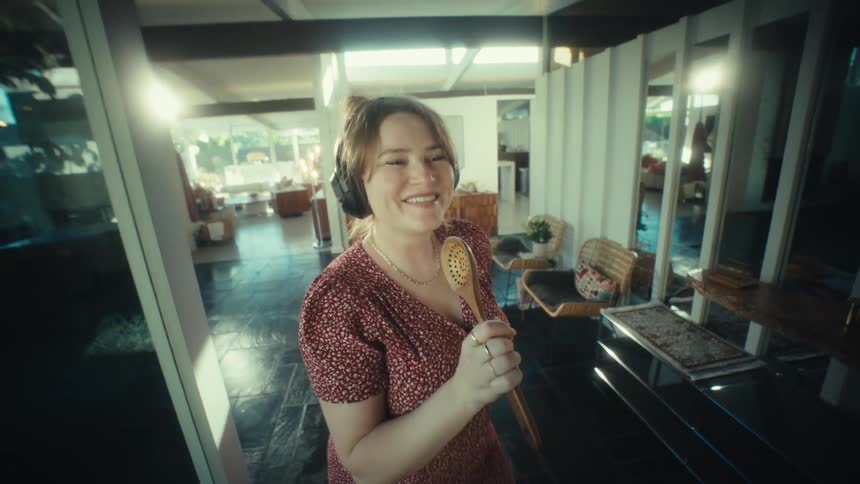Woman singing with headphones and wooden spoon in a home setting