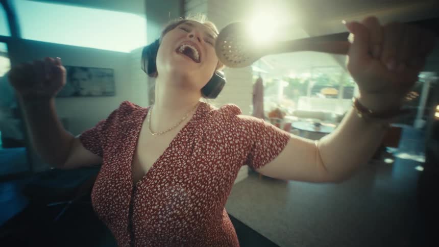 Woman sings at home using a spoon as a microphone on a sunny day
