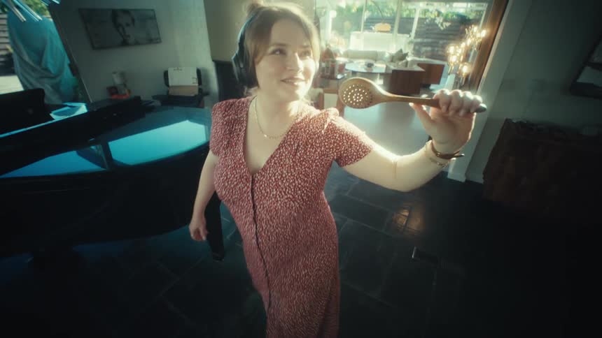 Woman wearing headphones holds a hairbrush as a microphone while walking through the room