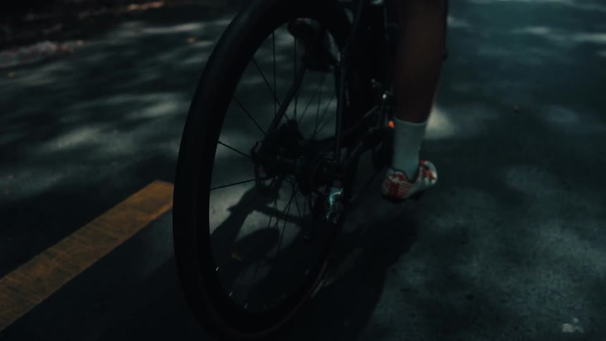 A cyclist rides a road bike along a paved path with dappled sunlight