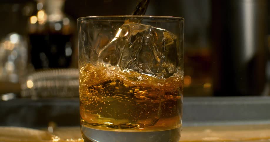 Drink pouring from a bottle splashes on an ice cube in the glass