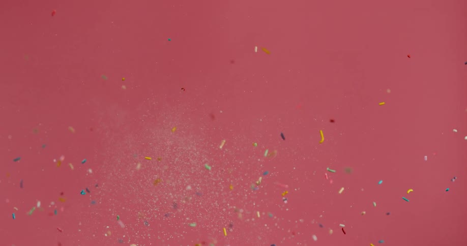 Frosted donut flies through the air as sprinkles also fly through the air